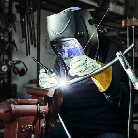A craftsperson welds metal while wearing a protective mask and gloves