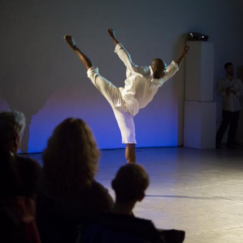 a lanky dancer dressed all in white sprawls through the air in front of a projector