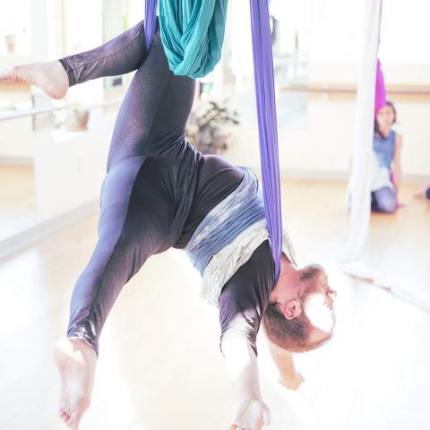 Toby suspended upside down in aerial silks in a brightly lit studio