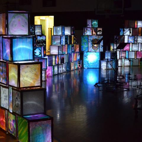 Illuminated cubes are stacked on top of each other in various pyramid/wall formations within a cavernous dark space.