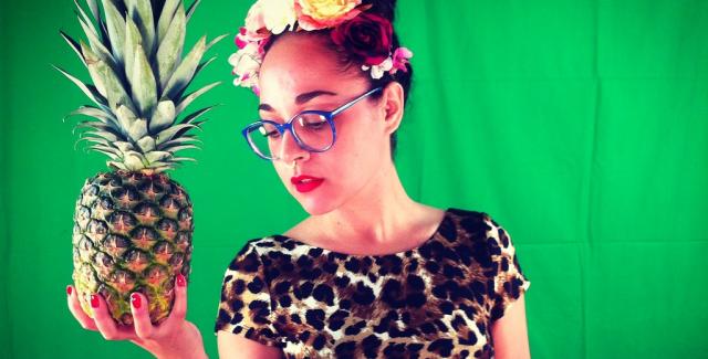 Paloma poses in front of a green backdrop with a pineapple in her hand.