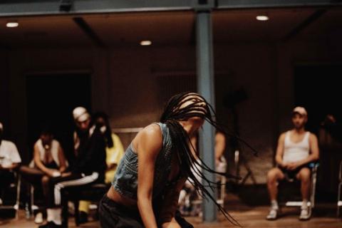A person with long braids spins around and folks watch in the background.