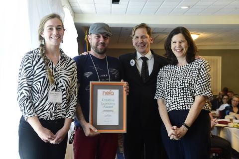 4 people stand shoulder to shoulder; one holds framed award that reads NEFA's Creative Economy Award