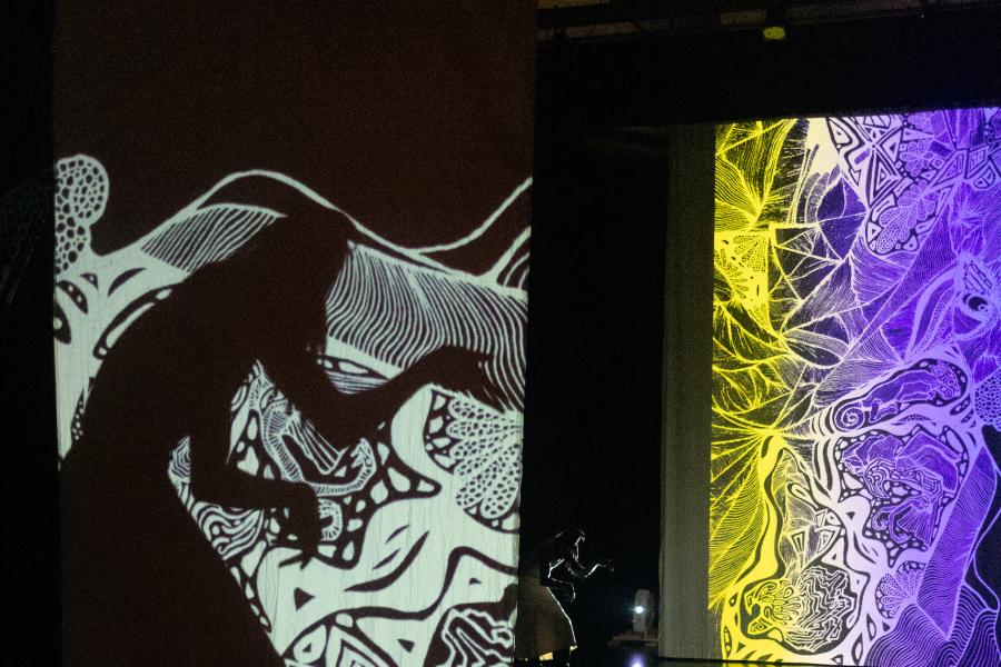 A projection of illustrated mountains is interrupted by the shadow of a dancer with their shoulders hunched and arms forward.