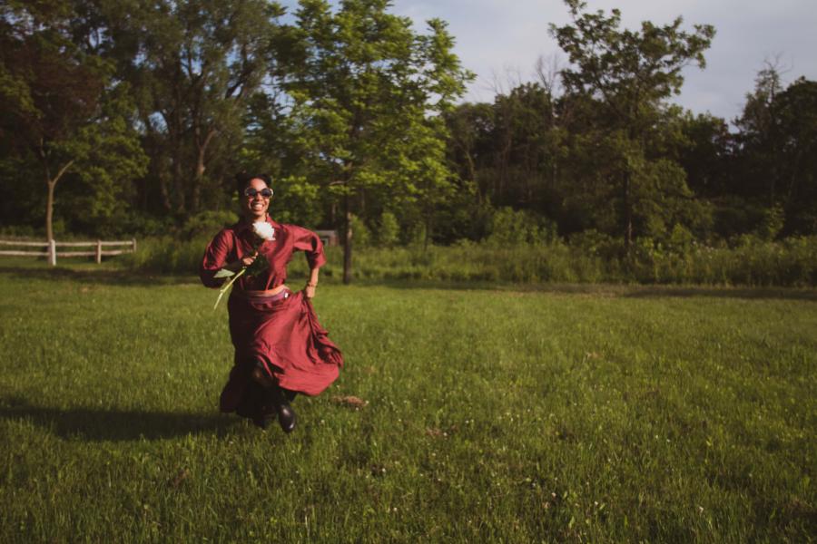 A woman, in a shiny red dress, runs through a field.