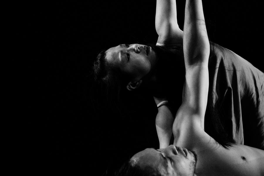A female dancer seems to pull an imaginary string that tugs the arm of a male dancer.