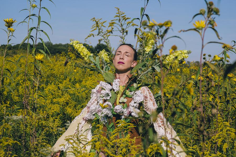 A white woman stands in field, intertwined with tall flowers.