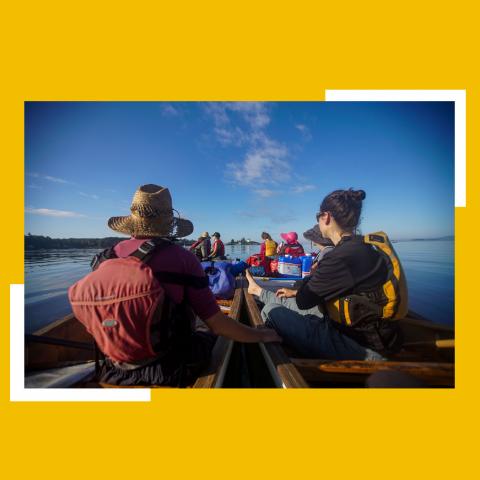 From the canoe, ten canoers travel along the coast on a sunny day.