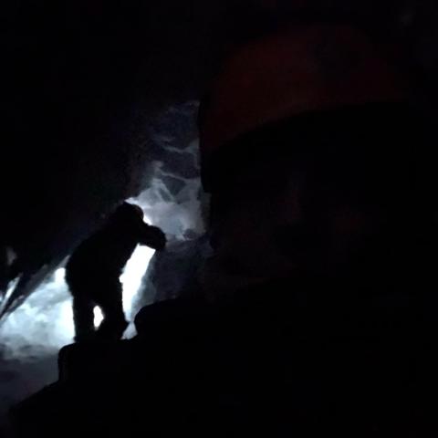 In a cave, a person with a flashlights climbs rocks.
