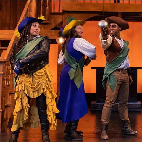 On a stage, four actors of color are dressed as muskateers.