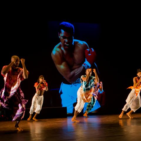 Four dancers perform in front of a projection of Muhammad Ali.
