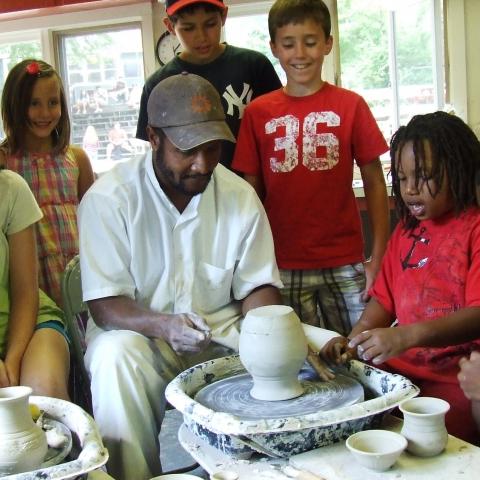 Sculptor demonstrates how to use a pottery wheel to six students