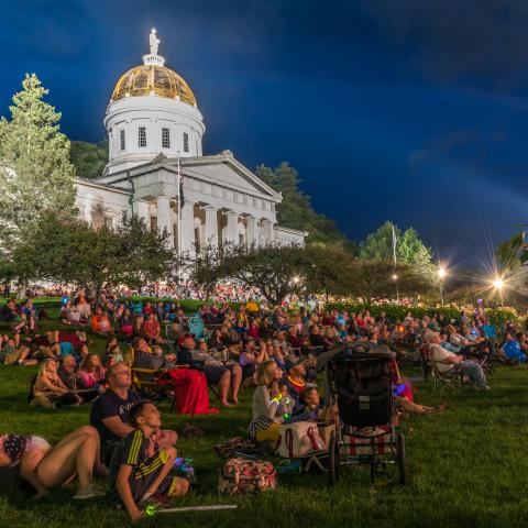 A crowd lounging on the lawn of the Vermont state capitol building 