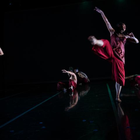 Three dancers, in red outfits, leap.