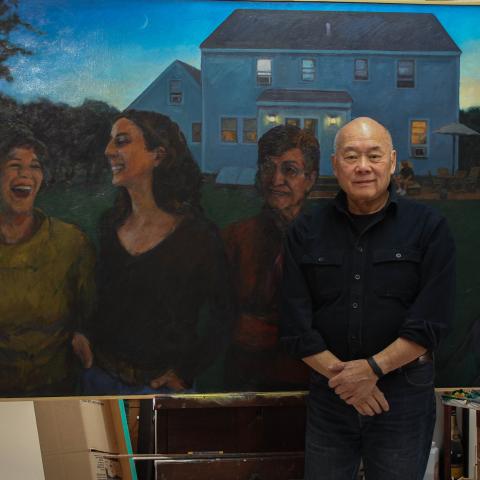 Wen-ti poses in front of one of his painting. A painting of women in the yard of a house at twilight.