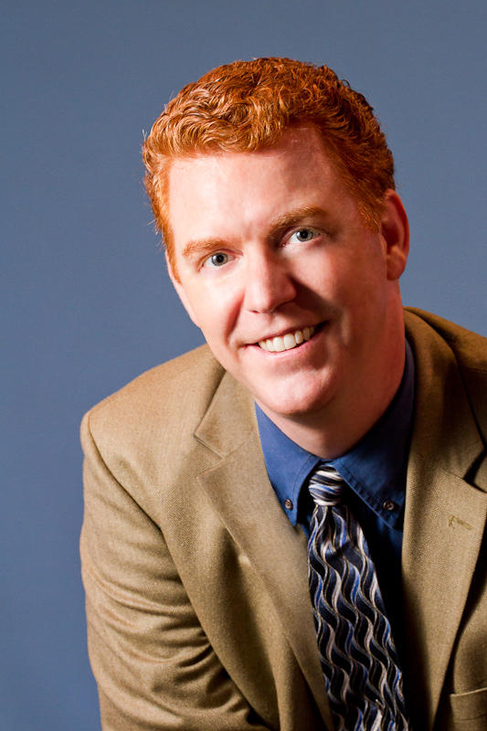 Charles leans forward in front of a blue-gray background
