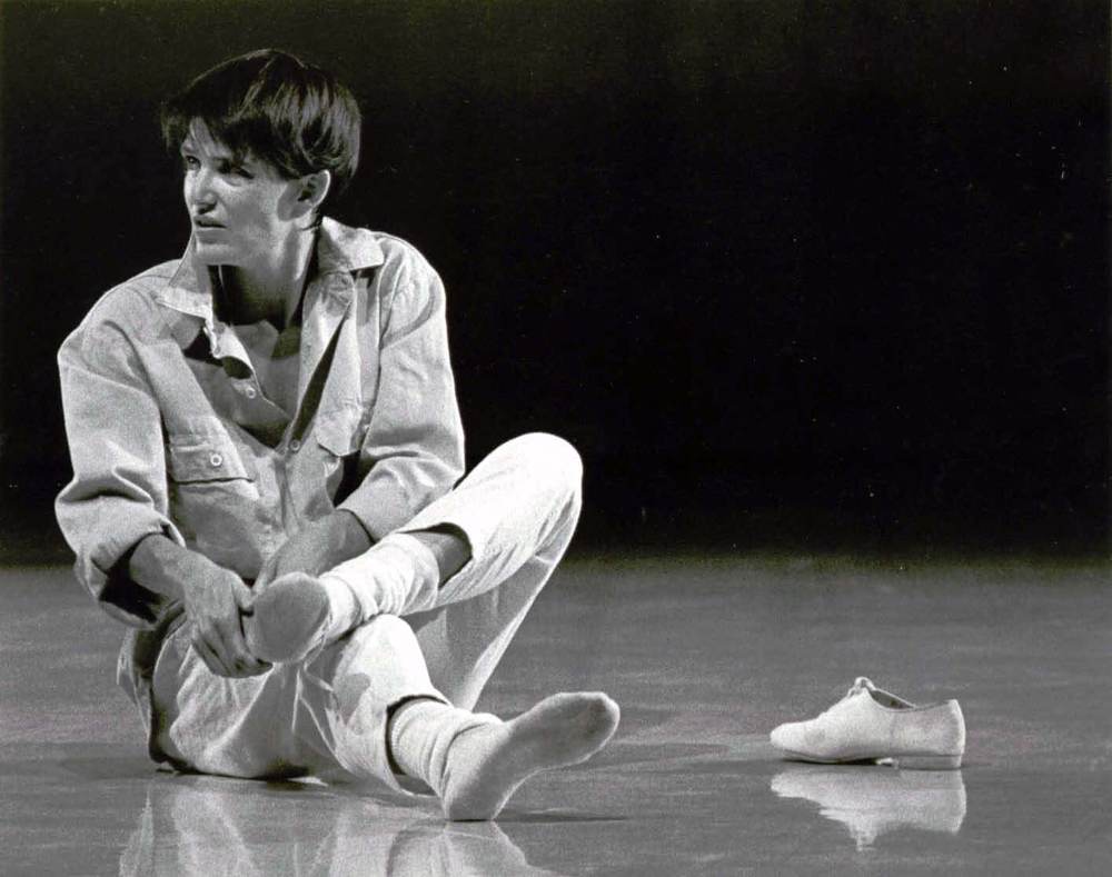 Polly sits on the floor with her shoes off, rubbing her feet