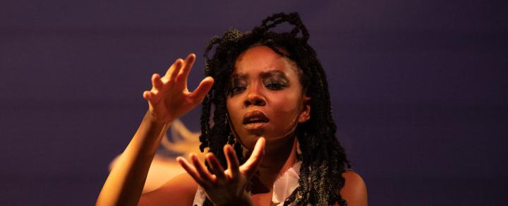 A Black woman, with long braids, holds her palms up facing each other.