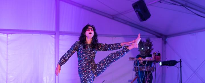 An Asian woman, with long black hair, holds her left leg up and wears a sparkly one piece that covers her full body.