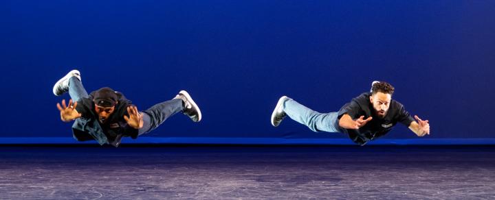 Two men of color appear to float over the stage like superheroes, mid jump.