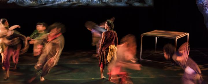 On a stage, one figure stands in focus and the rest have motion blur all around them.