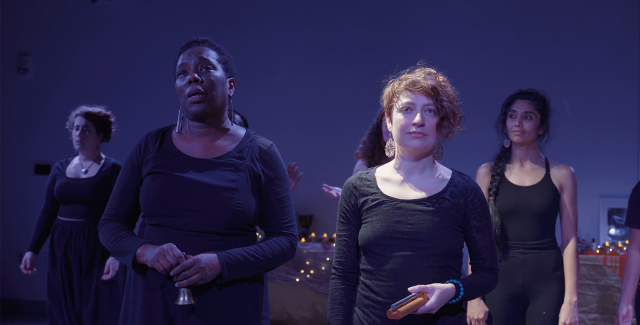 On a stage, in black outfits, black, brown, and white women smile and look around.