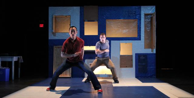  Two performers on a blue and white set. One performer slightly more in the foreground than the other.