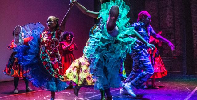 Six folks of color, in neon gowns, dance in spotlights.