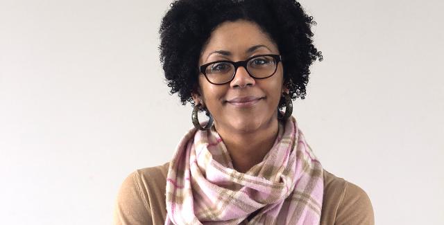 Ashleigh crosses her arms and smiles in front of a gray wall.