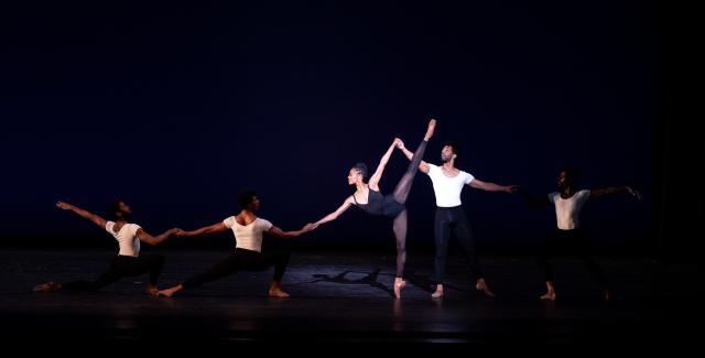 On a stage, dancers performer ballet in black and white unitards. 