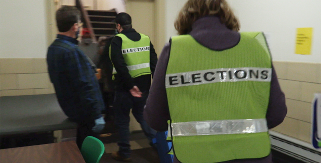 Folks, in vests that read "elections" on the back, walk towards a stairwell.