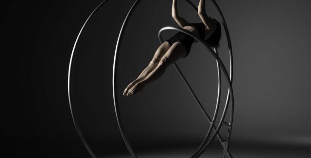 A white person, in a Black bikini, hangs from a round metal bar that envelopes their body.