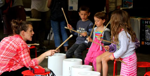 Maria teaches three kids how to use buckets as drums.