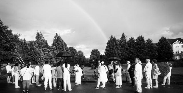 A group of folks stand in a parking lot next to a rainbow.