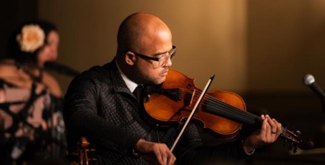 In a spotlight and a checkered jacket, Daniel plays the violin.