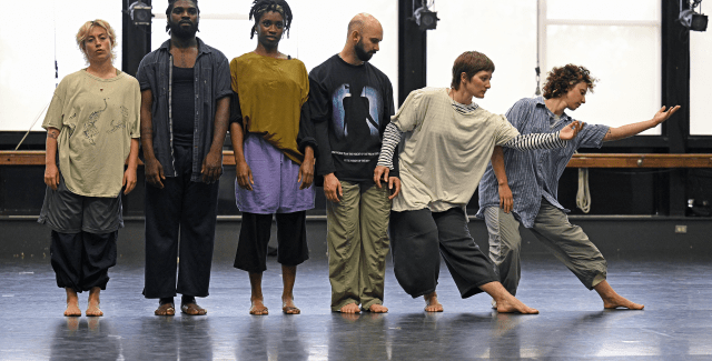 Six people stand in a land. Four of them stand still while the two on the right dance.