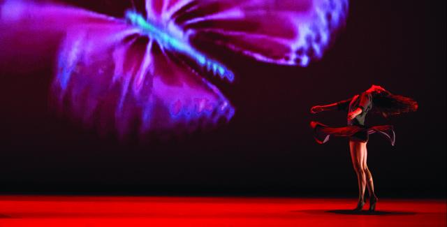 A female dancer spins next to a projection of a very large butterfly.