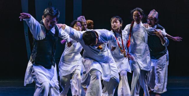 A group of performers dressed in white dance together on a stage.