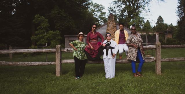 Five black women pose by a log fence.
