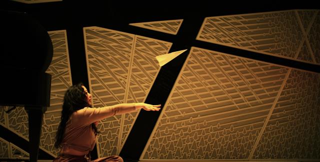 In a room with padded walls, a woman throws a paper airplane.
