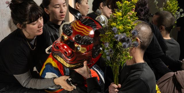 Folks, in black clothes, hold an east Asian dragon mask and leaves.