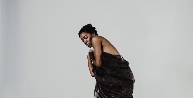 A person stands in front of a white background wrapped in a dark cloth.