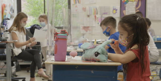 Young students wear N95 masks and sit at their desks.