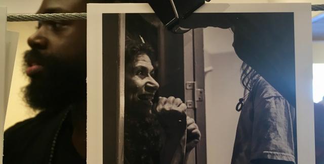 A man stands behind a drying print of a black and white photo of Melissa looking in a mirror.