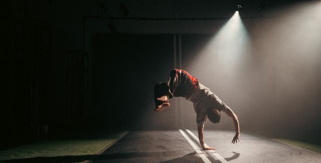 In a spotlight and on a road that appears to continue up the wall, a dancer does a flip.