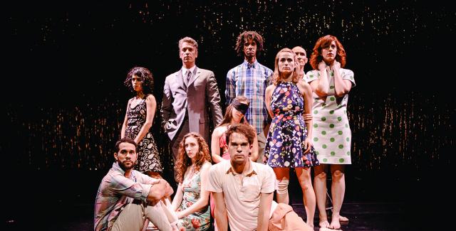 Ten dancers in everyday garb pose in front of a wall metallic streamers. Ripped cardboard and a baseball bat lay in front of them.