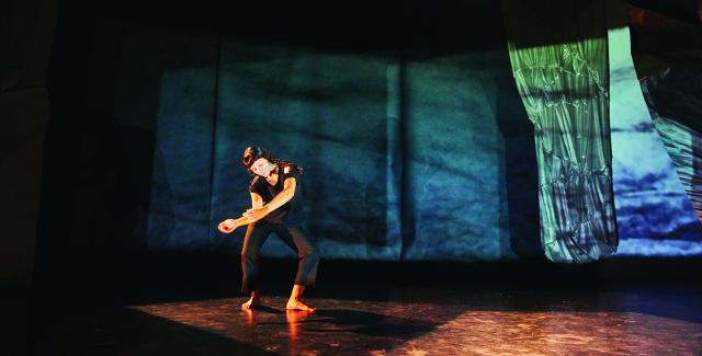 Woman in black dances in front of a blue and green projection of a texture.