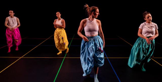 Four dancers, in monochrome, but each different, parachute pants, perform in a black box with the same colors as intersecting lines on the ground.