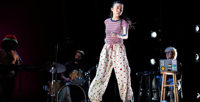 An Asian woman, in baggy pants, walks across a stage.