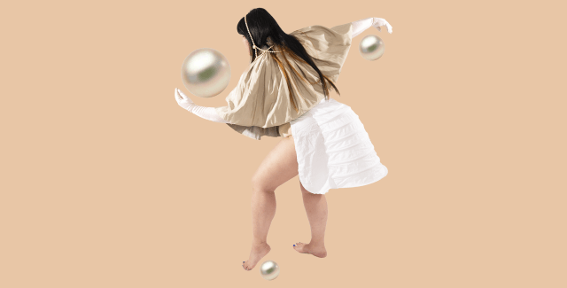 In front of a tan colored background a long haired person wearing a golden top stretches out their arms to the front and back. Three pearls of great size are shown by their hands and left foot.